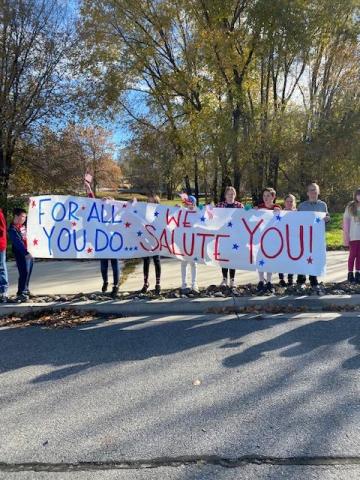 Students holding a sign that says " For all you do, we salute you!"