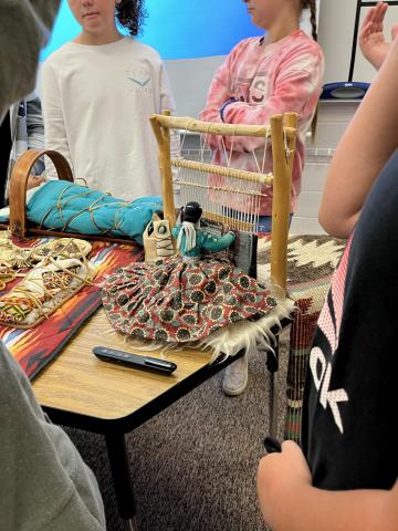 Fourth graders looking at mini replicas/models of how Native Americans weave blankets